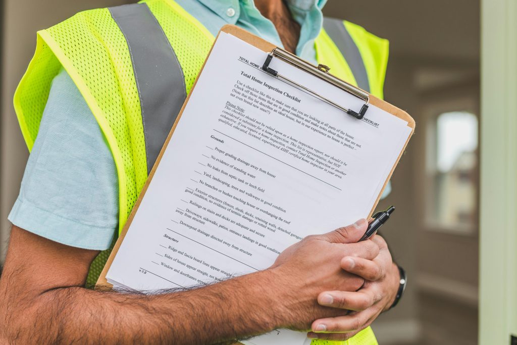 A home inspector in a reflective safety vest holding a pen and inspection checklist
