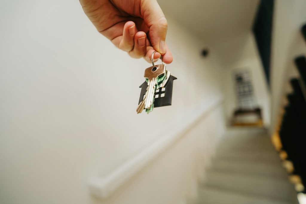 A hand holding a house key in front of a home's entrance
