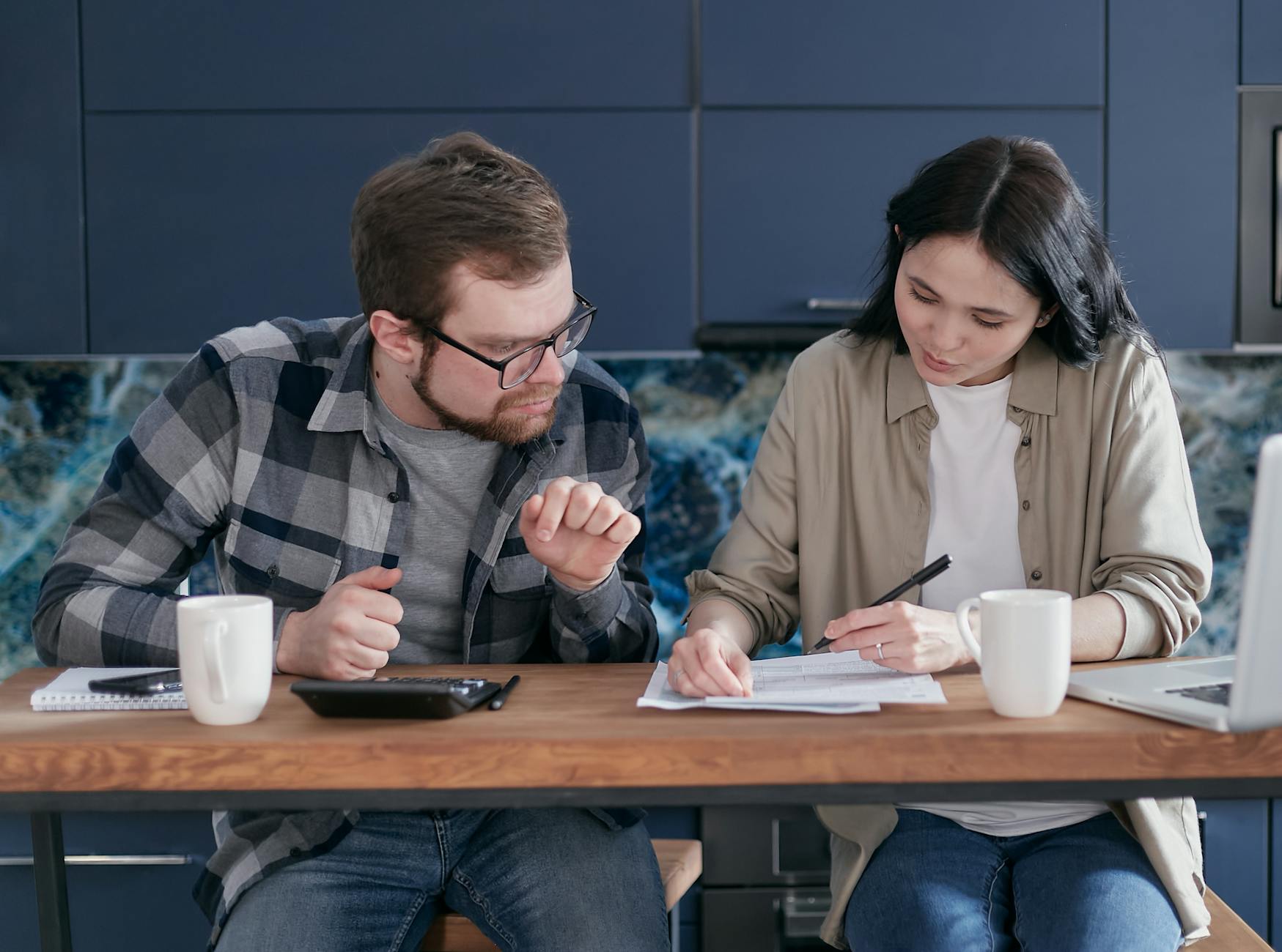 Couple at a kitchen table with paperwork and a laptop, weighing a financial decision — the rent-vs-buy conversation made real.