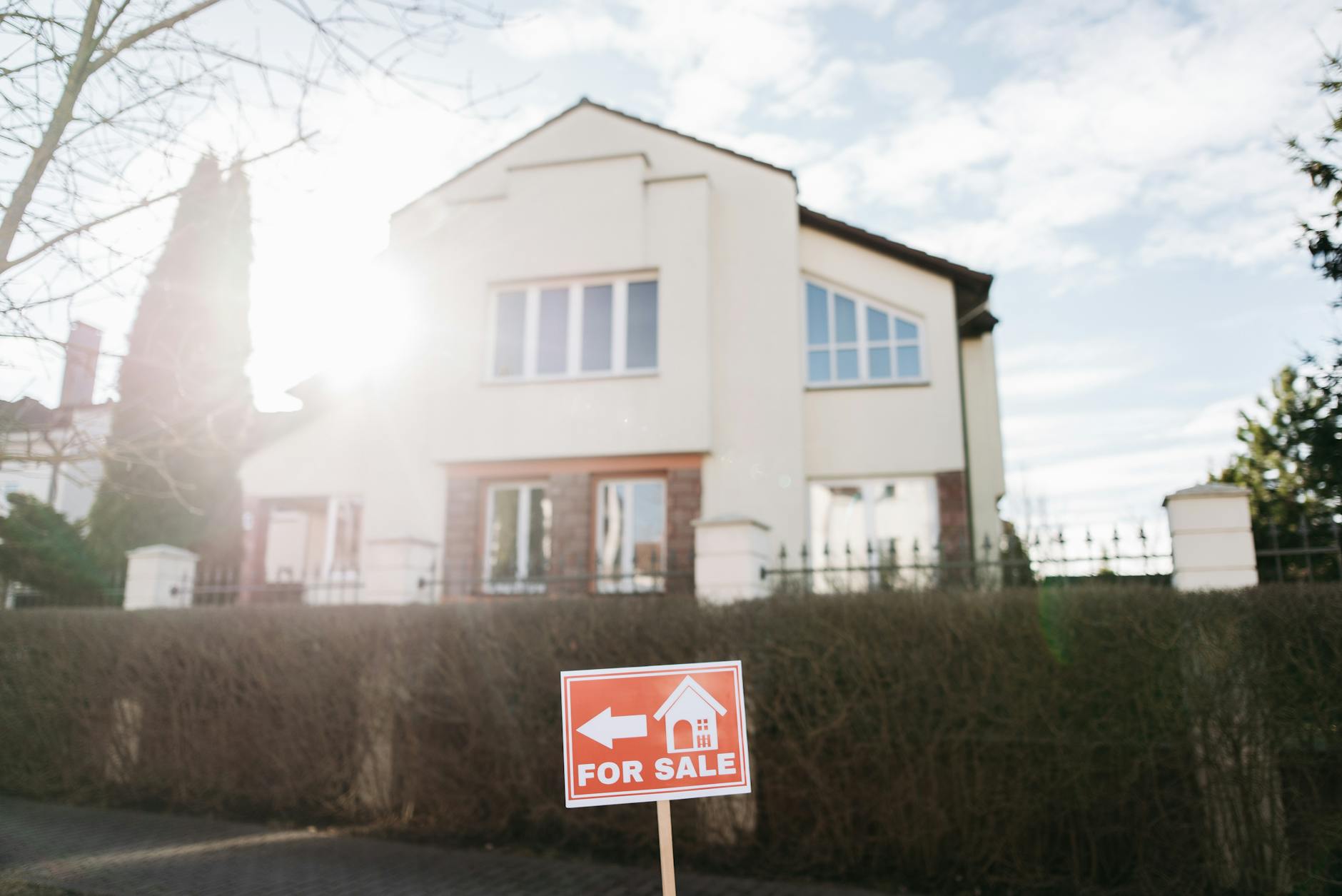 Suburban home exterior with a for-sale sign — the owning side of the comparison.