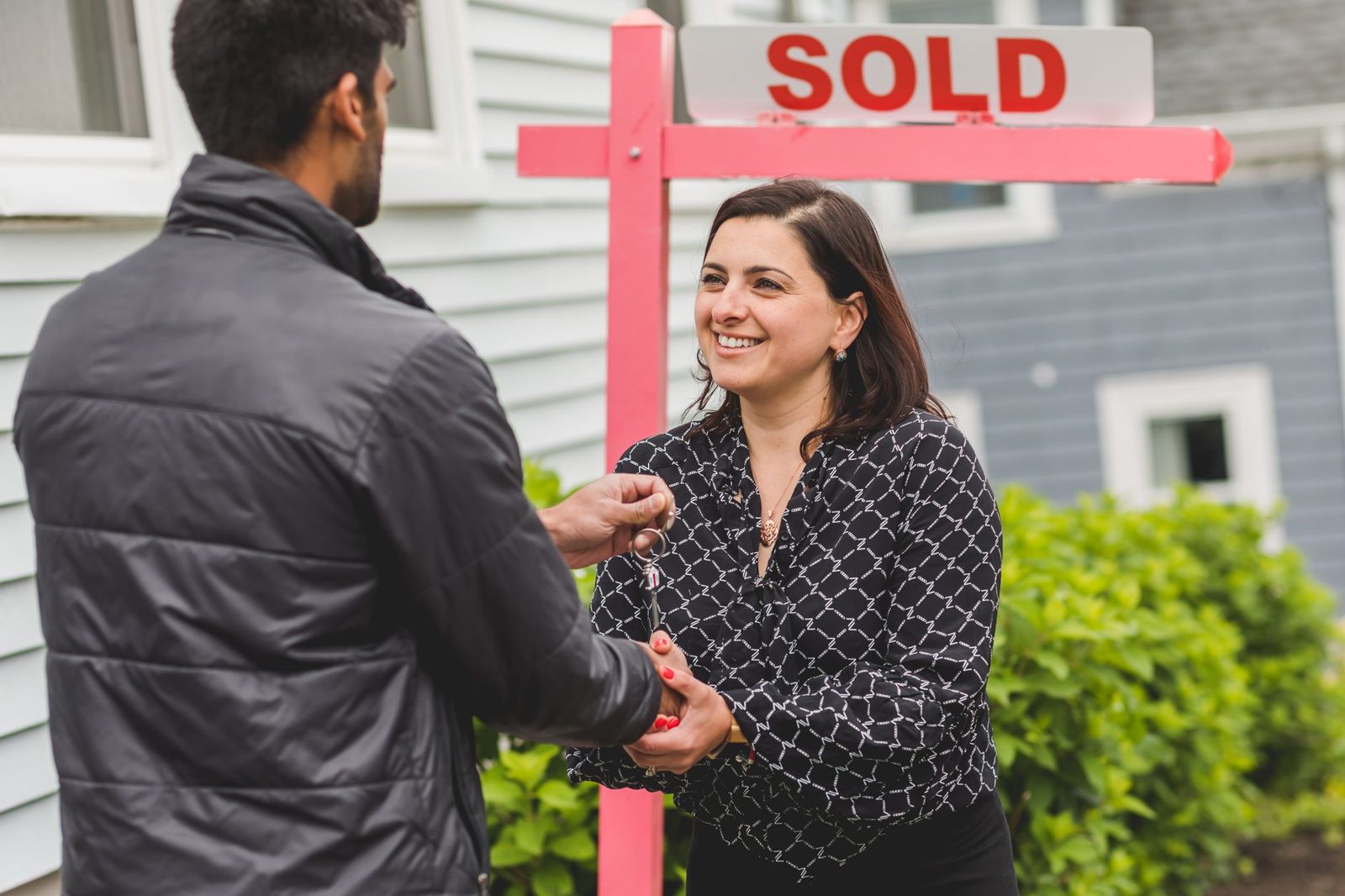 Homebuyer shaking hands with agent outside a coastal home after closing