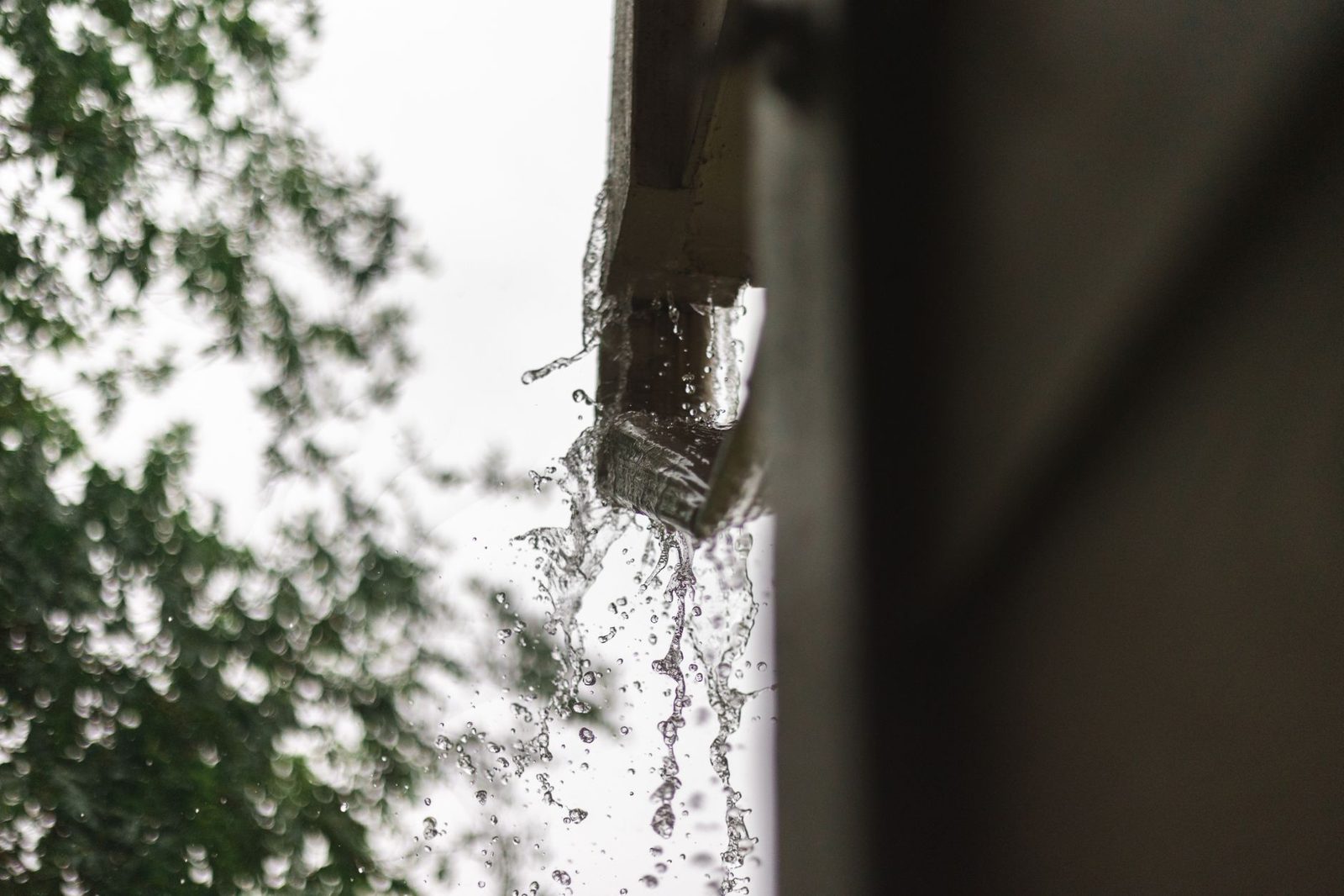 Water overflowing from a gutter during heavy rain near a house foundation