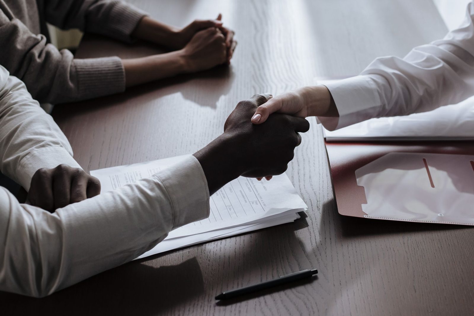 Two people shaking hands over paperwork at a table after reaching an agreement